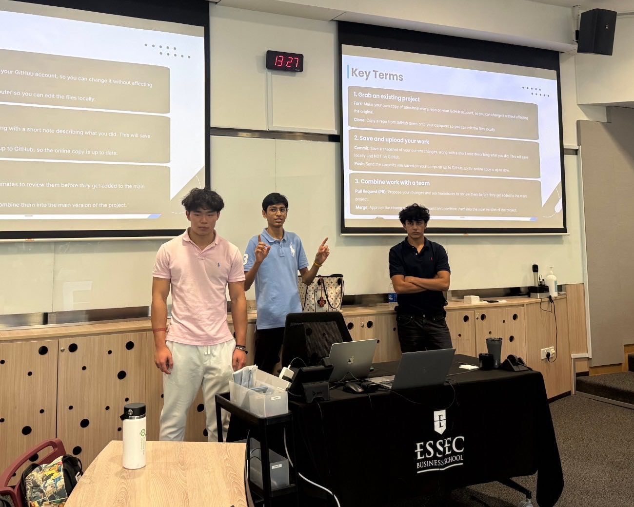 Yibo, Nirvan and Rishabh at the front of the lecture room, in front of a slide of GitHub key terms.